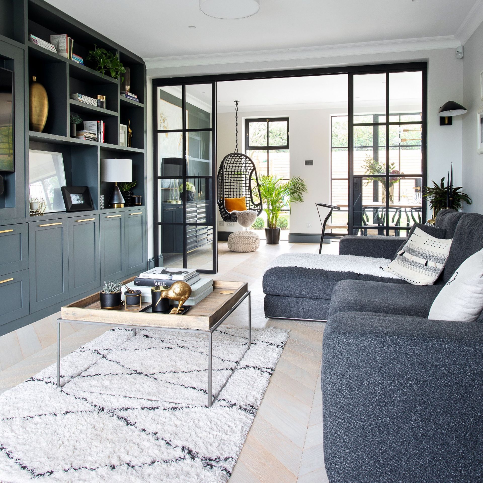 The viral 'blue sofa' controversy dividing social media - Ideal Home 23 Dark blue sofa and fitted cupboards, pale rug, cushions and fabric throw, view through to the dining area with hanging chair and dining table