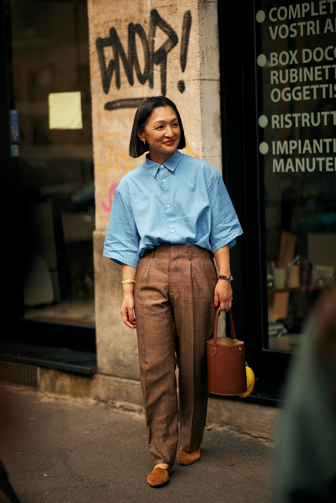 Mens Fashion Week SS26 showgoer wears a blue button-down short sleeve shirt with brown tailored trousers and brown velvet loafers