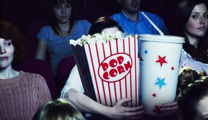 Woman holding giant sized popcorn and drink in cinema