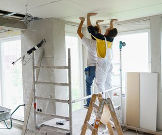 2 men dry lining a ceiling stood on small scaffold tower