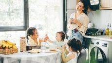 Tired mother drinking coffee while watching three kids sitting around the breakfast table