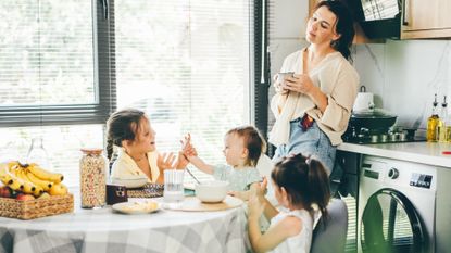 Tired mother drinking coffee while watching three kids sitting around the breakfast table