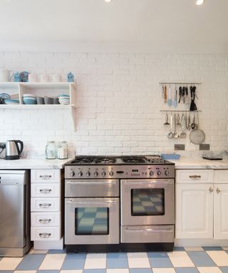 An image of a large silver oven in a kitchen with white cabinets, white walls, and blue and white tiled floors