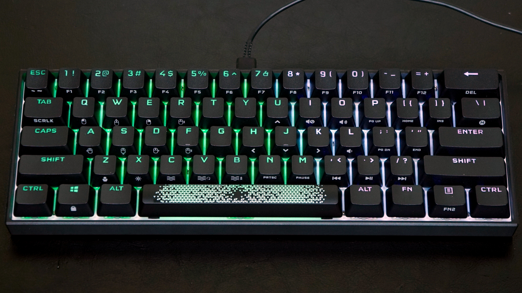 Et Corsair K65 Mini-tastatur ligger på et sort skrivebord.