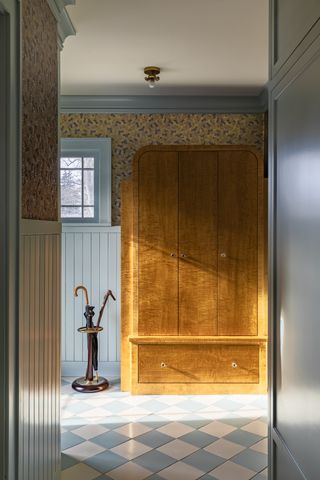 A pale blue panelled hallway with detailed wallpaper and large wooden cupboard at the end