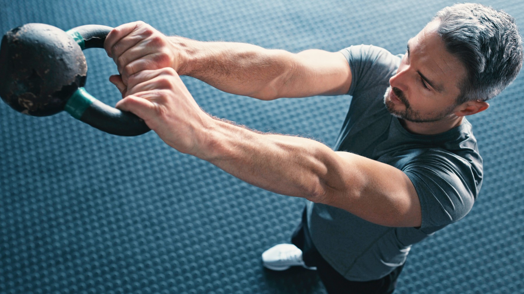 Muscled male swinging a kettlebell overhead gripping weight with both hands and arms extended