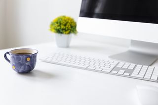 A tidy white desk with a plant, a mug of coffee, and an iMac.