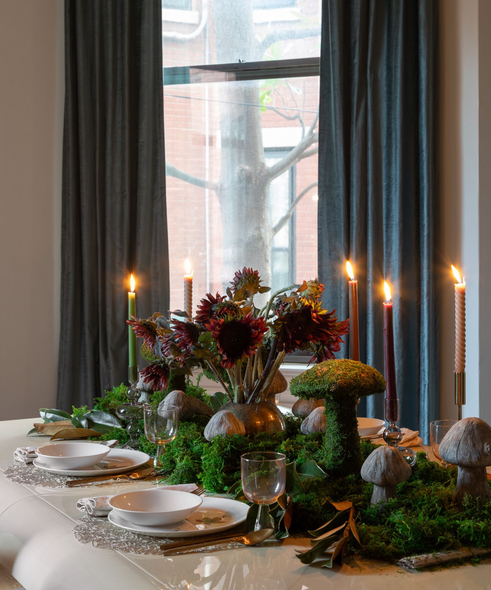 neutral dining room with teal curtains hung over a large window and a white table styled with mushroom decorations, moss, fall flowers and taper candles
