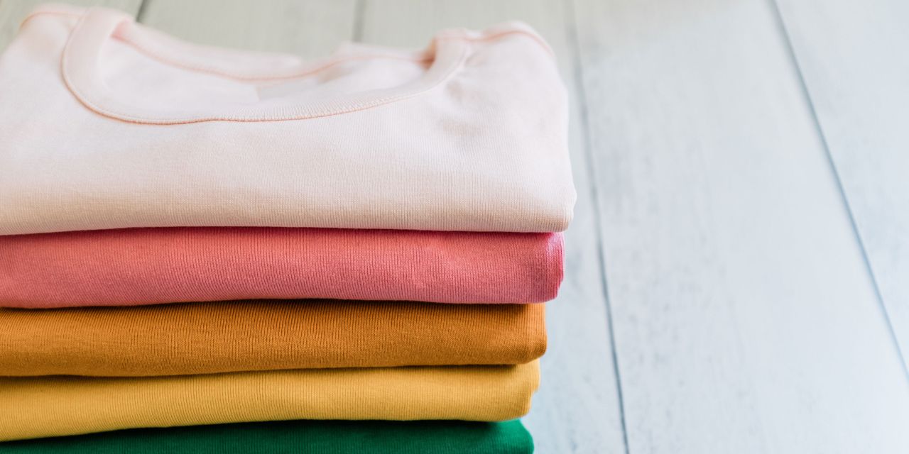 a stack of colourful tshirts on wood floor - GettyImages-1273553051