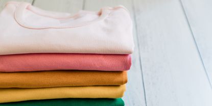 a stack of colorful tshirts on wood floor - GettyImages-1273553051