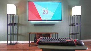 A mouse and keyboard in front of a TV with the Framework Desktop in the left corner of an entertainment center