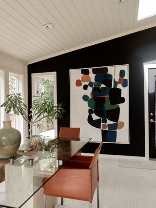 black and white dining room with large modern artwork, vaulted ceiling, shiplap, glass dining table, leather armchairs, pale patterned carpet