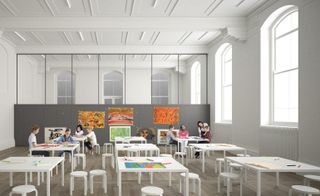 An art classroom with white square tables and stools. Lots of light floods the area from the tall windows on two sides.