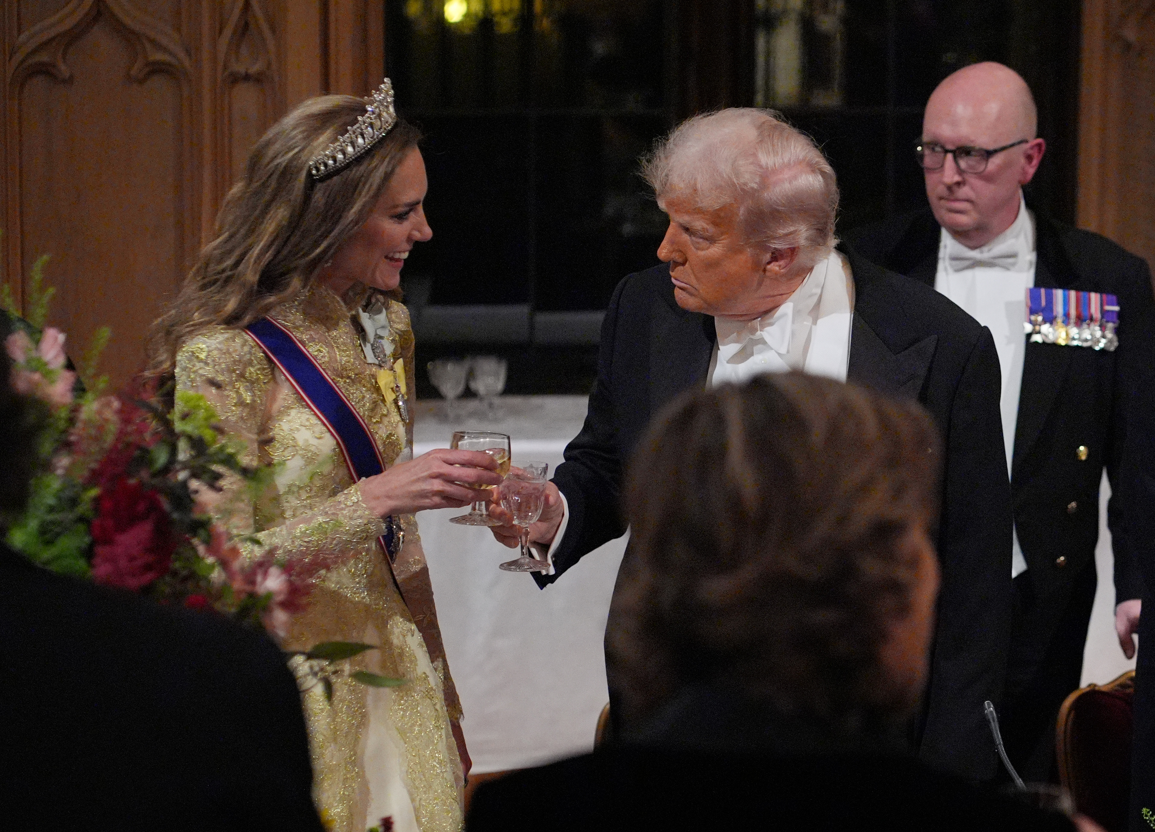 Kate Middleton wearing a gold dress toasting to Donald Trump at a banquet