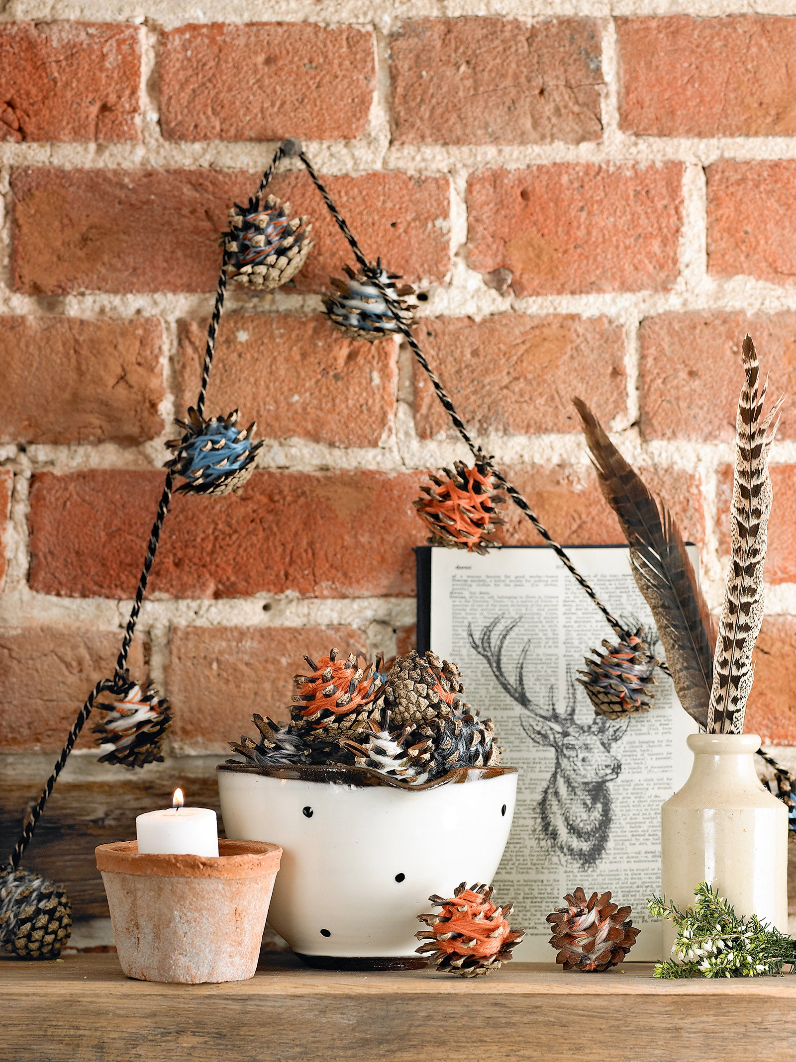 Handmade pine cones displayed on a string to make a decorative garland on a brick wall.