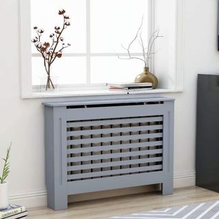 Grey radiator cover with slatted front underneath window with vase of twigs and cotton stems