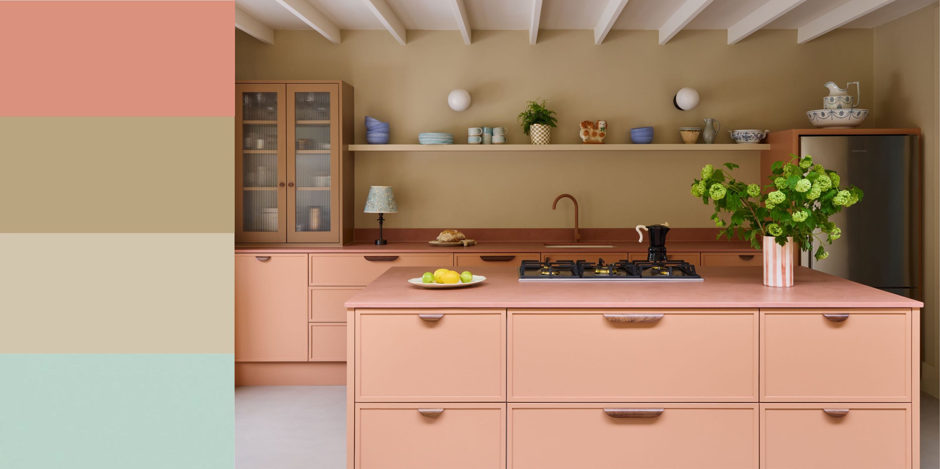 A modern kitchen with salmon pink cabinets, sandy beige walls, a caramel brown wall cabinet, a pink kitchen island, light grey flooring, and a white ceiling. 