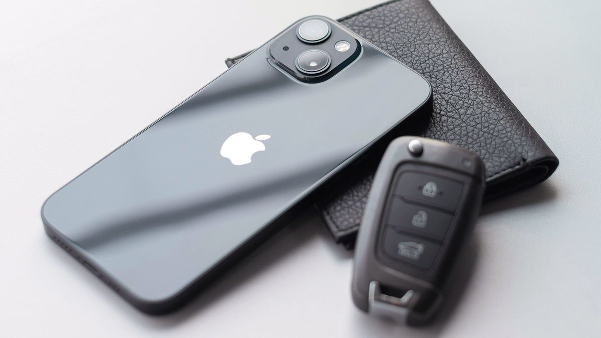 An iPhone, a wallet and a car key on a counter top.