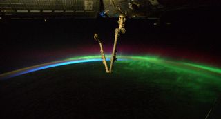 A photo of a green, blue, and purple aurora in the background, with the Canadarm2 robotic arm in the foreground