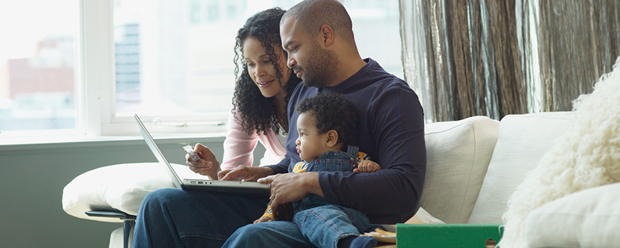 Black American family, husband and wife reviewing finances while holding their baby sitting on a couch. 