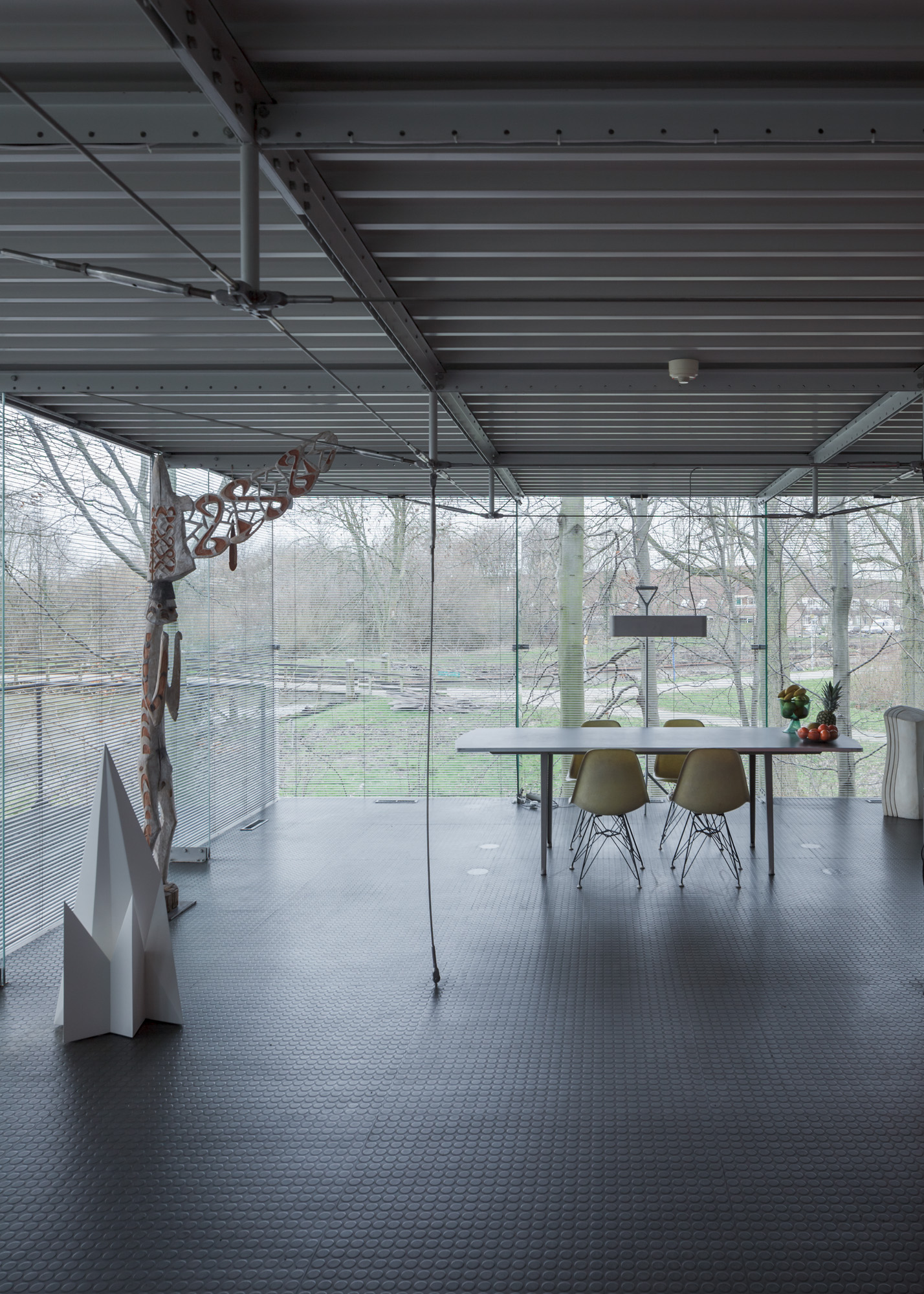 the dining room has floor-to-ceiling windows on two sides. the floor is black and there is a white table with off-white chairs.