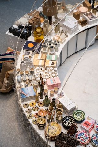 A furniture shop sited in a brutalist, industrial location features a semicircular product display table filled with all sorts of home accessories in glass and ceramic.