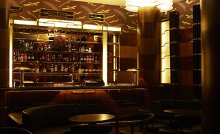 A restaurant bar area with leather sofas, wooden chairs, a bar counter, a glass liquor display cabinet and airplane patterned wallpaper.