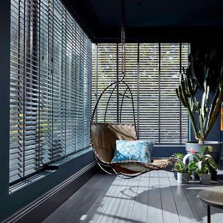 living area with wooden floor and teal grey wall with large windows with venetian blinds and swing chair