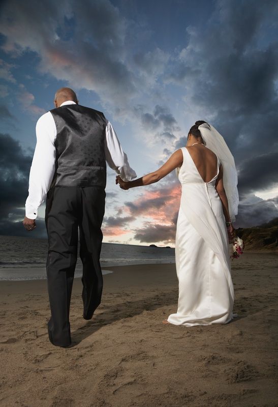 A newlywed couple walks on the beach.