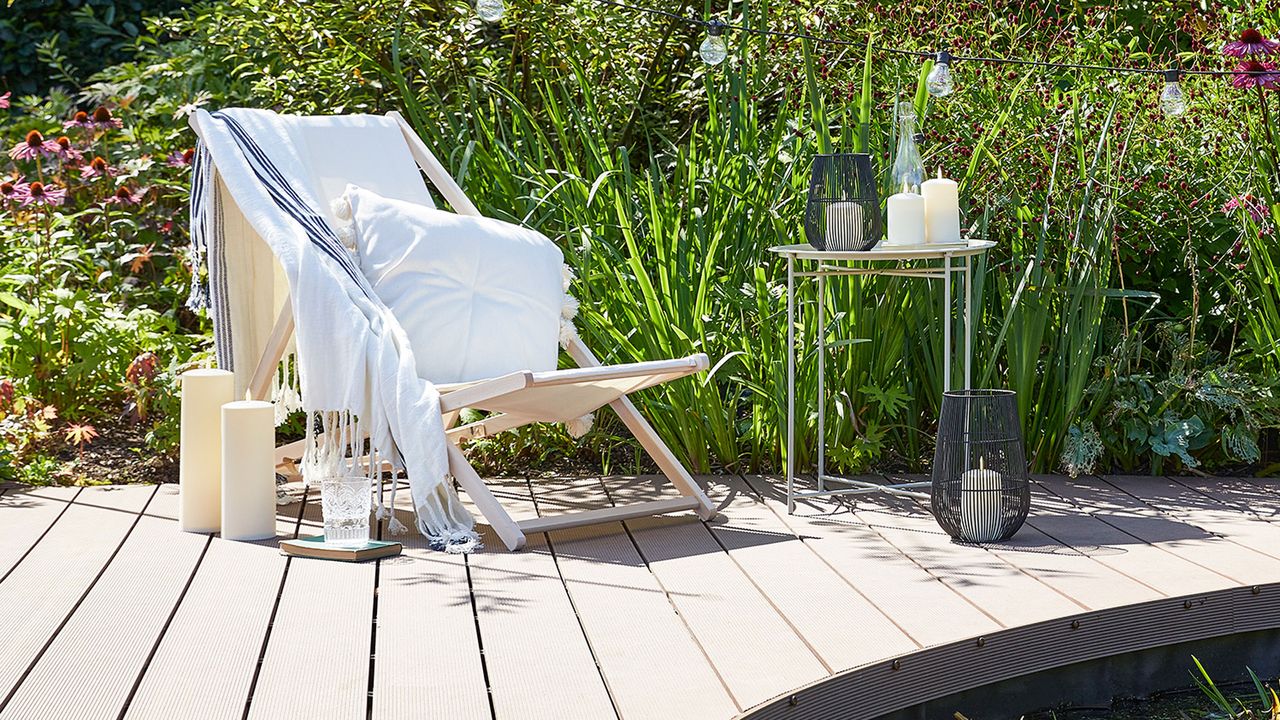 composite decking in outdoor space with tall green plants, a deck chair, festoon lights and candles