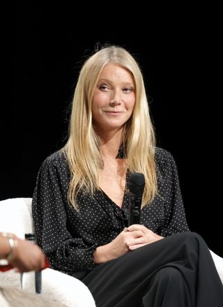 Gwyneth Paltrow with long layered blonde hair holding a microphone and wearing a black and white polka dotted top.