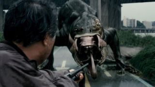 Scene from the movie The Host (2006). Here we see a close up of a man pointing a large gun at an alien creature who is on all fours with a giant mouth full of teeth.