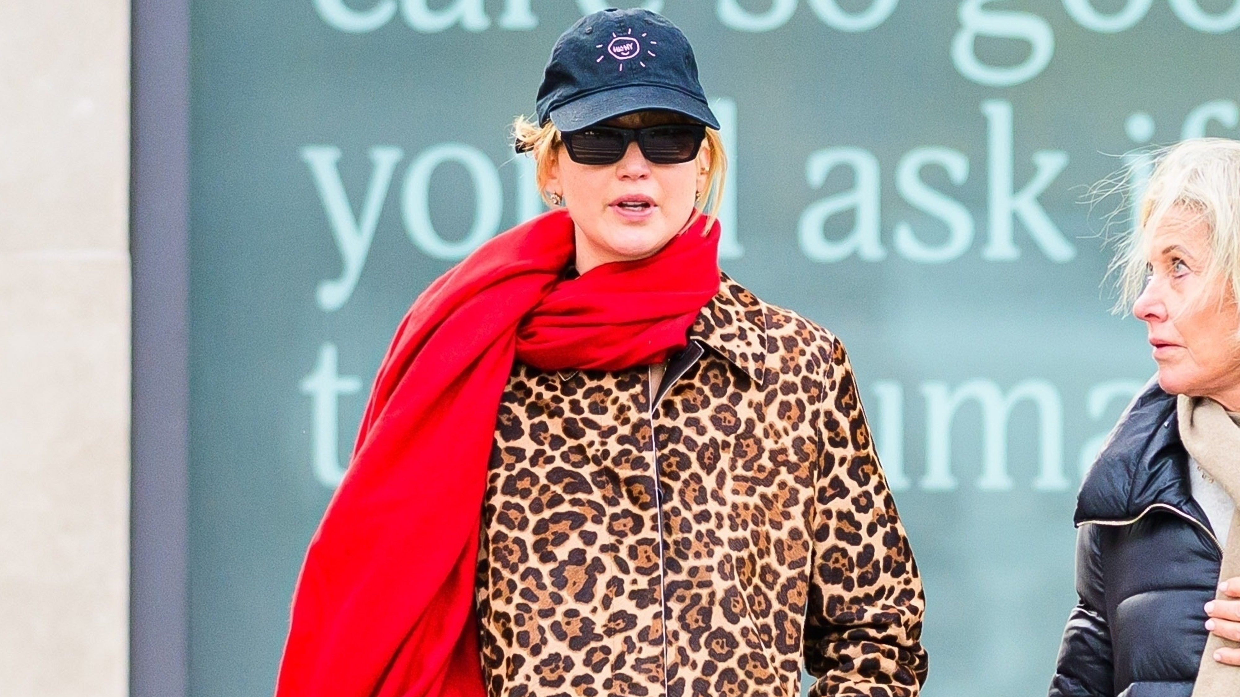 Jennifer Lawrence wears a baseball cap, red scarf, and leopard-print coat.