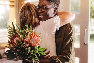 A man and a woman are embracing, the man is holding a bouquet of flowers.