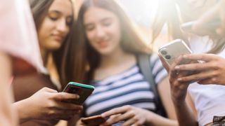 Teens stand in a circle, each looking at their phones with smiles on their faces