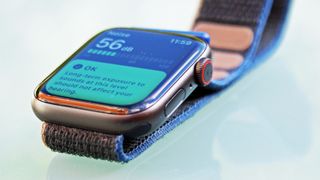En Apple Watch SE med ett blått och brunt armband ligger på ett glasbord och gör en ljudmätning.