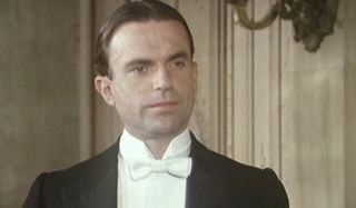 Reilly Ace of Spies Sam Neill dressed in a white tie tuxedo, half smiling in a parlor