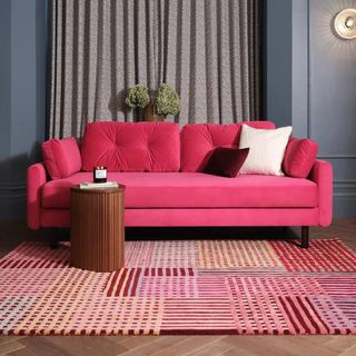 A bright pink sofa in front of a pink striped rug
