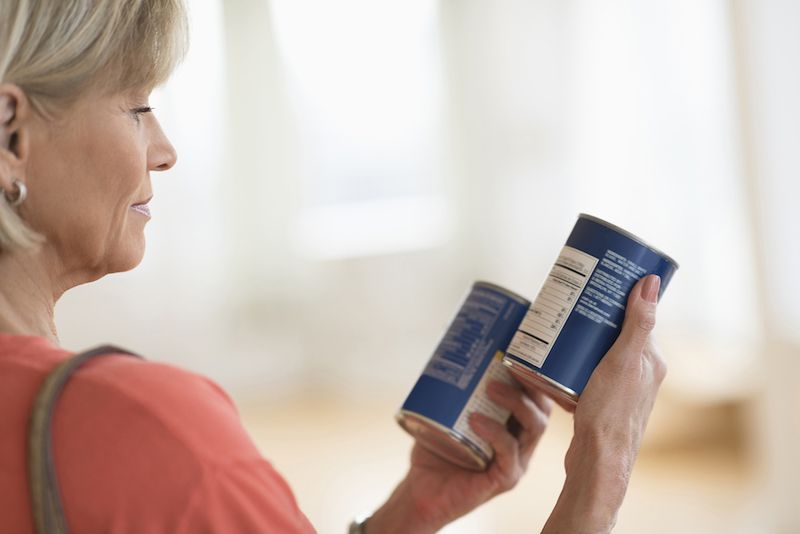 A woman reads food labels while grocery shopping.