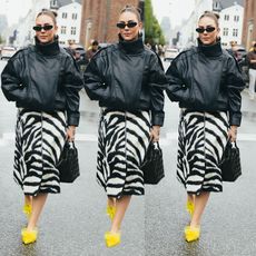 Woman wears black leather funnel neck jacket, leopard print skirt and yellow heels. 