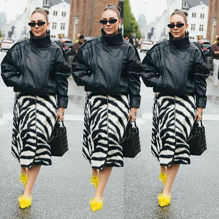 Woman wears black leather funnel neck jacket, leopard print skirt and yellow heels. 