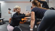 Personal trainer in a gym corrects the form of a woman gym-goer holding a barbell