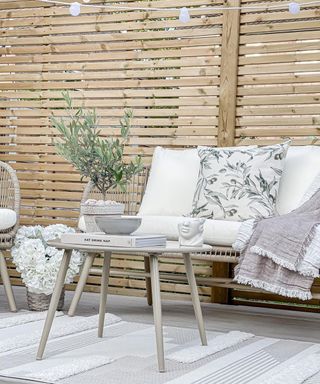 Mediterranean inspired deck with light wood fence, stone painted deck, white textured outdoor rug, an olive accessories