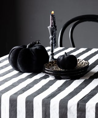 A dining table with a black and white striped tablecloth with pumpkins and plates on top of it