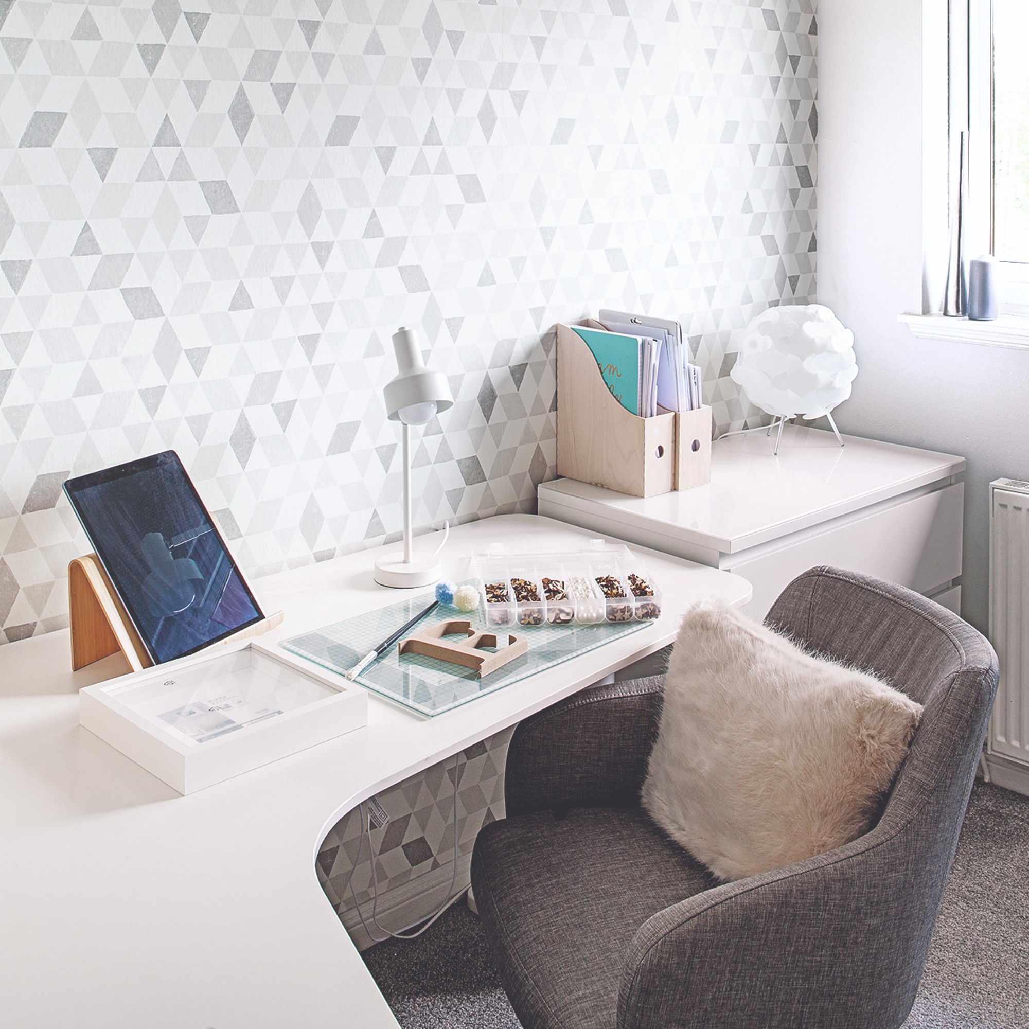 A bright home office with a corner white desk and a grey upholstered desk chair