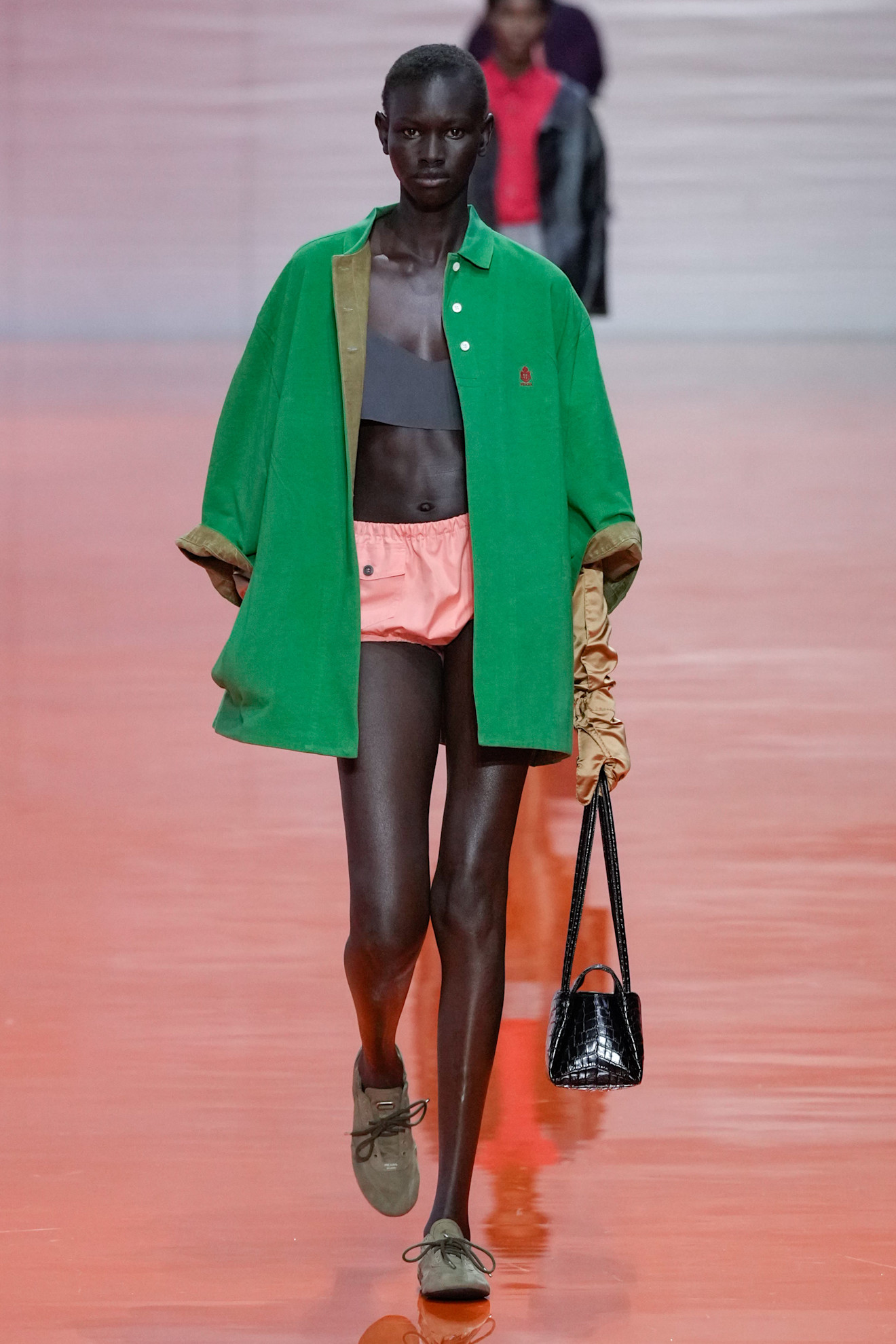 A model at the Prada SS26 show wearing a green suede polo-neck coat with a pink pair of briefs.