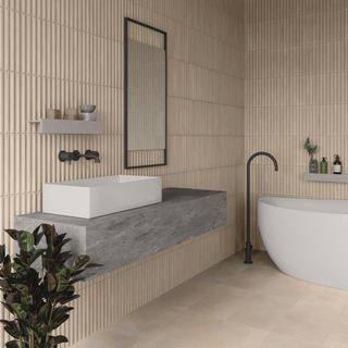 neutral wabi sabi style bathroom with textured tiled walls, stone floor, white bath, wall mounted vanity, small shelf, black fixtures and fittings