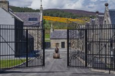 A man rolls a barrel of whisky out of the gates of a distillery