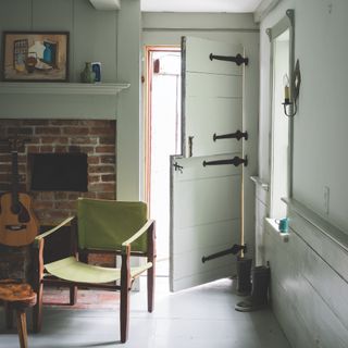 cottagecore decor ideas for living rooms, pale green cottage/farmhouse living room with stable door, directors chair, hearth, painted floorboards, brick fireplace, colour drenched walls in pale green