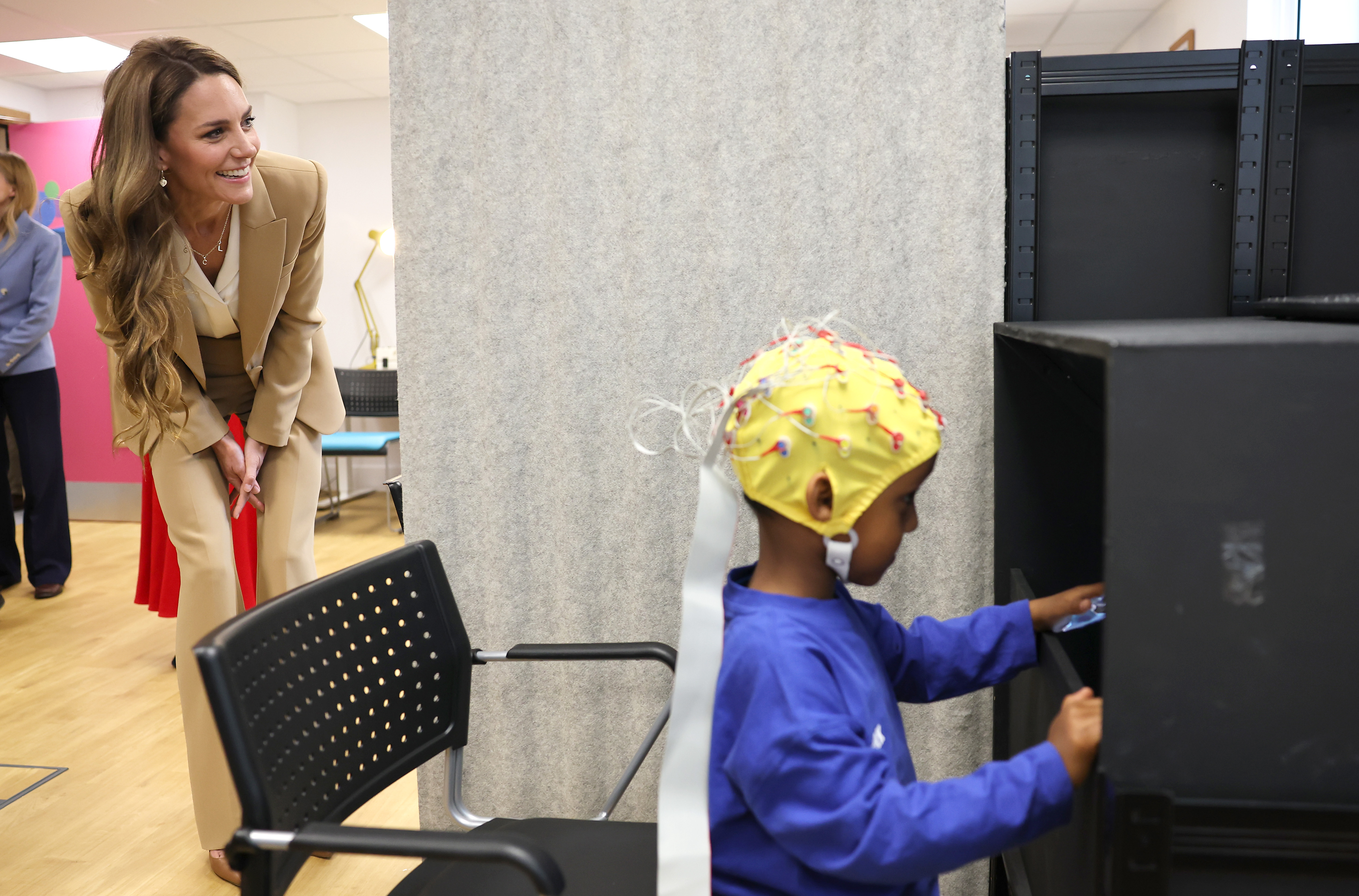 Princess Kate bends over and watches a child doing an activity